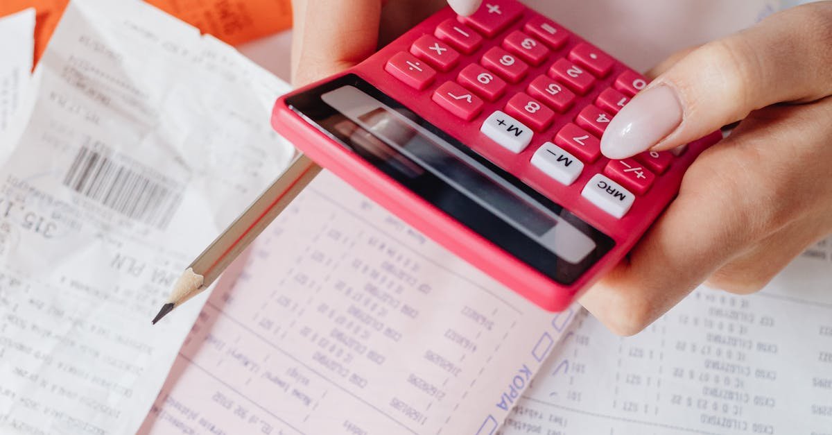 Hands using a red calculator surrounded by financial documents and receipts, symbolizing financial management.